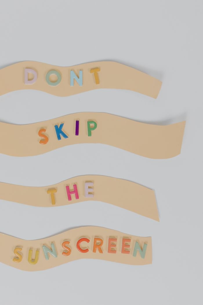 Vibrant letters spell 'Don't Skip the Sunscreen' on wavy strips, promoting skin health awareness.