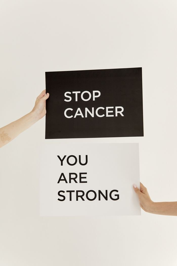 Hands holding inspirational signs promoting cancer awareness on a white background.