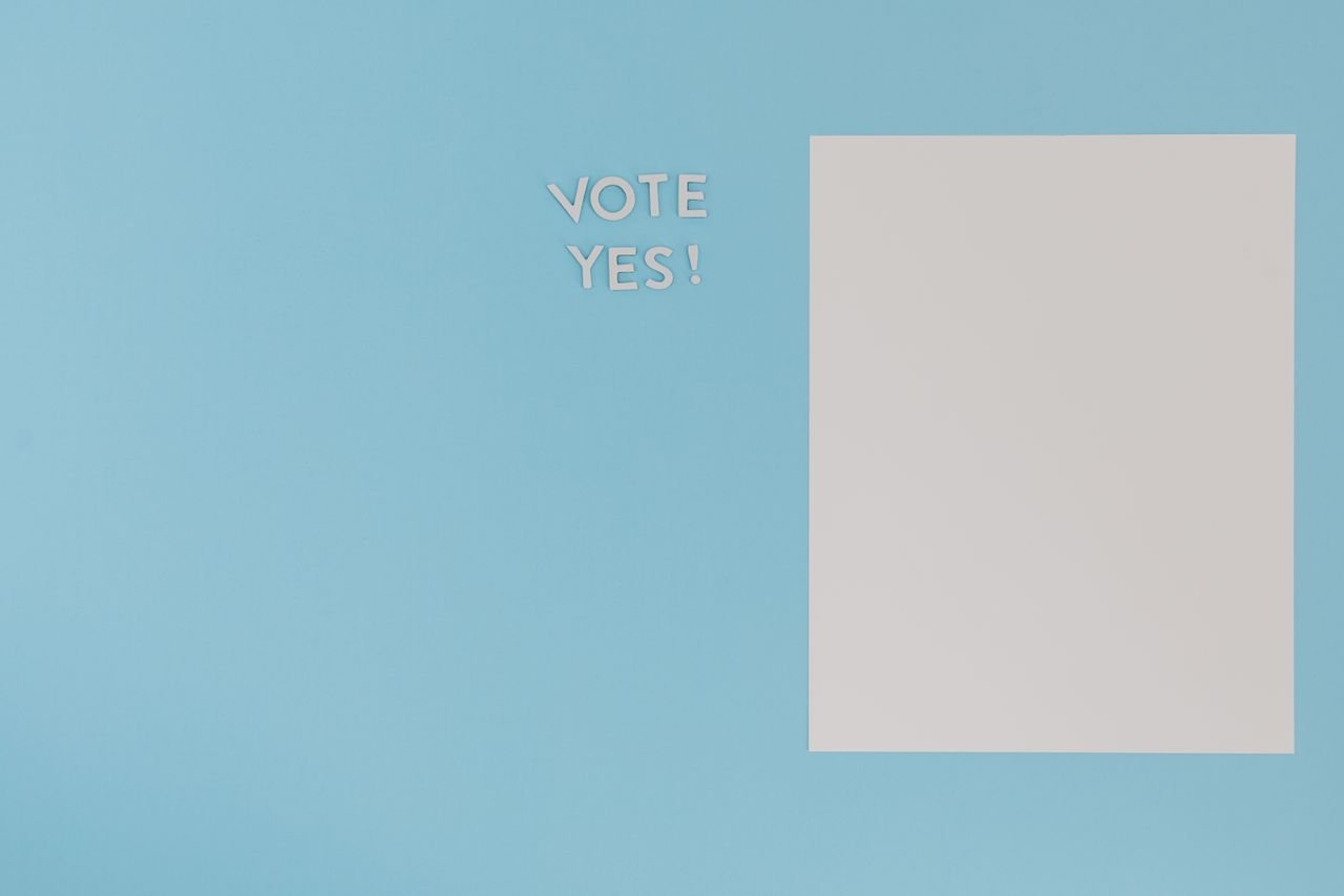 A minimalist concept image featuring 'Vote Yes' text and blank paper on a blue background.